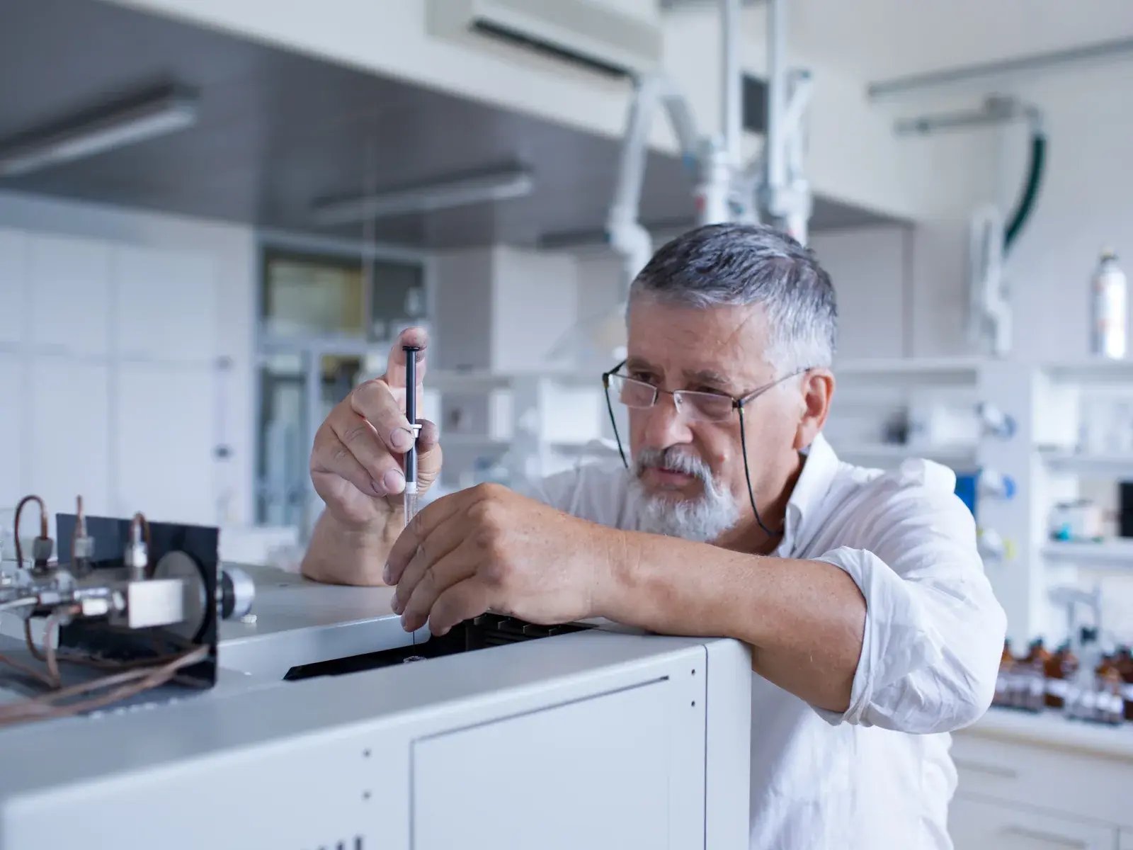 Senior researcher injecting sample into GC-MS instrument for forensic chemical separation and identification