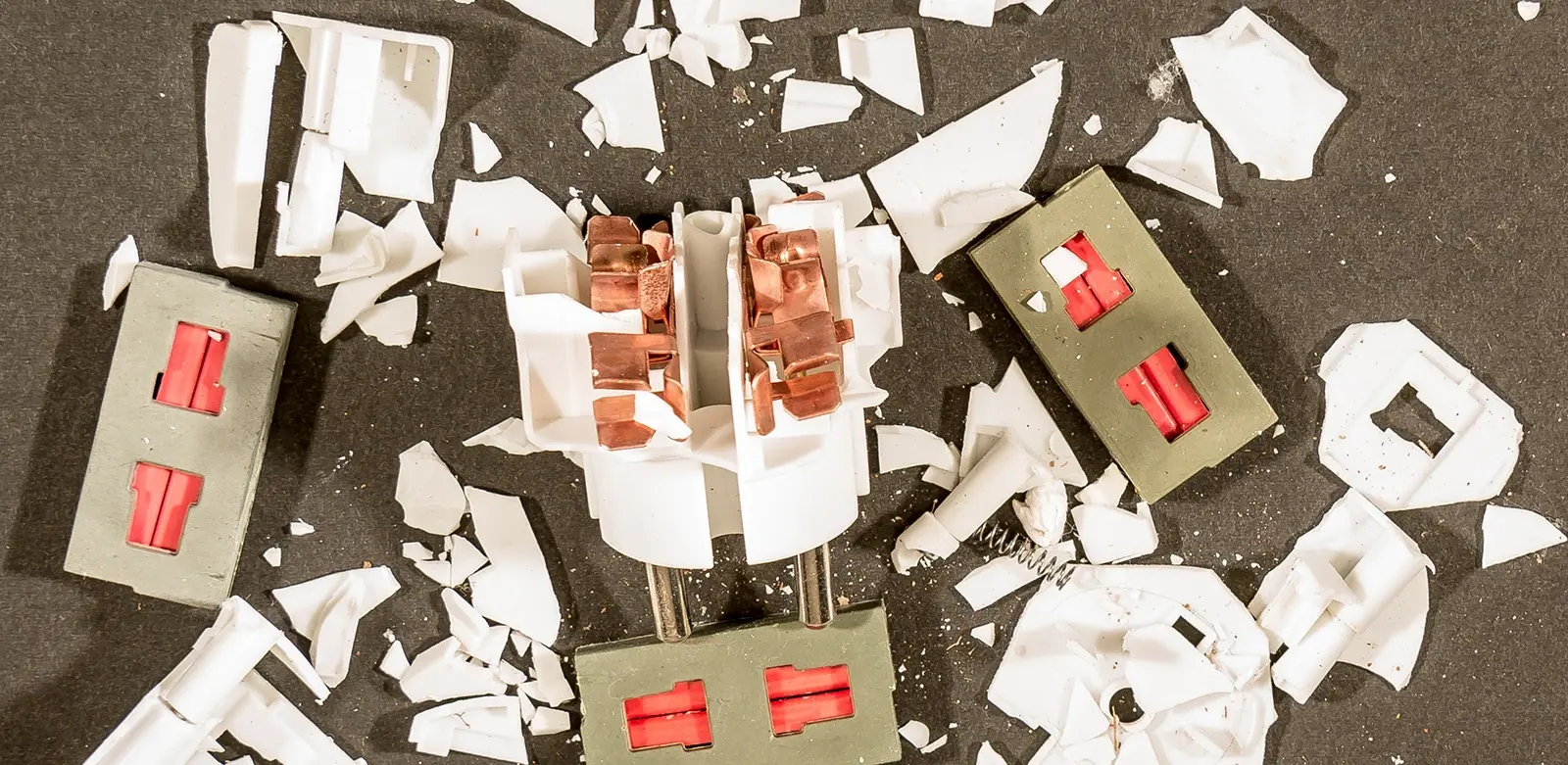 Shattered white plastic housing broken into fragments, exposing internal metal terminals