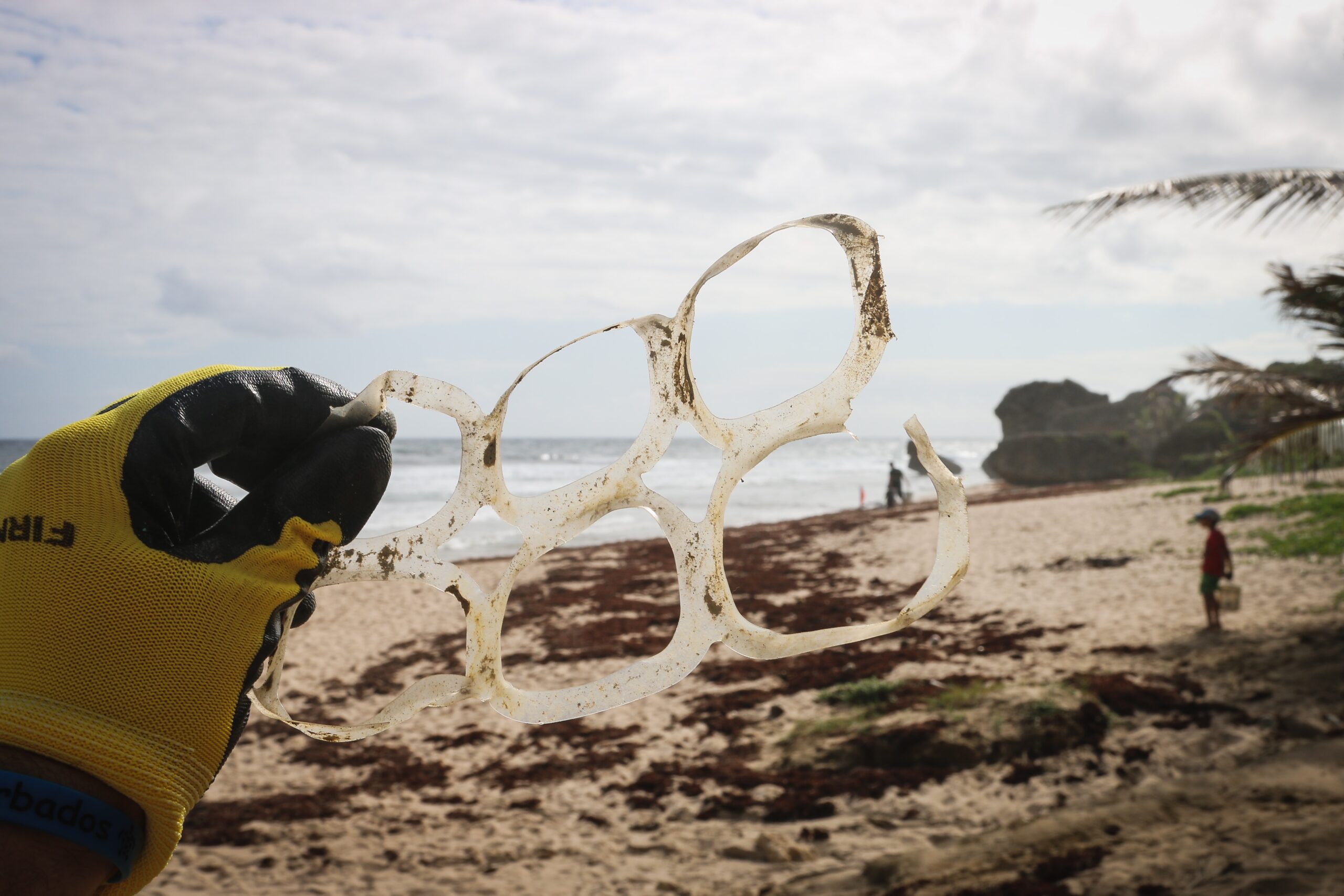 Gloved hand holding a discarded plastic six-pack ring carrier on a beach