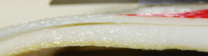 Close-up cross-section of the exercise ball wall showing the pale cellular material and a marked variation in wall thickness