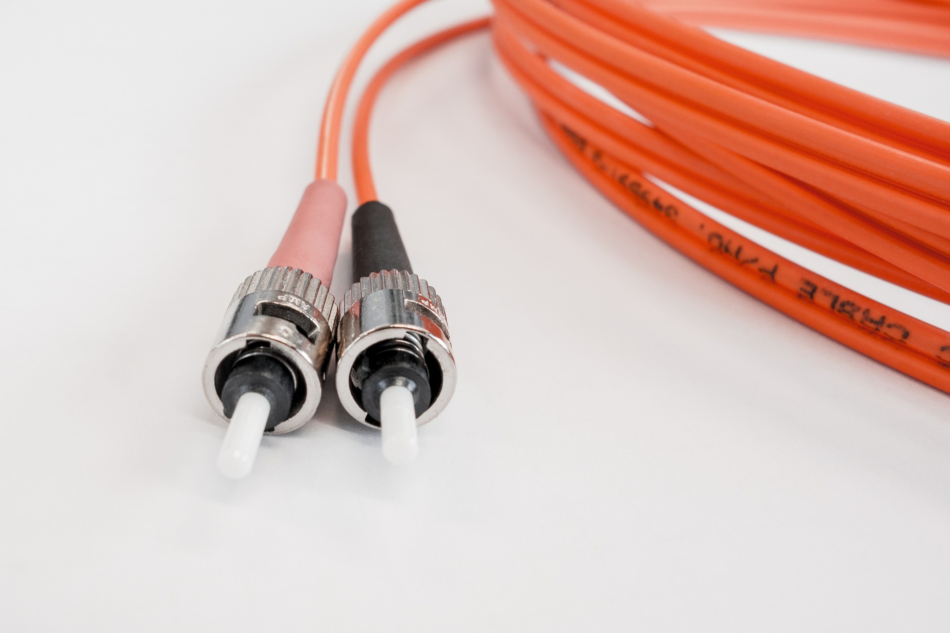 Coiled orange fiber optic patch cable with two connectors resting on a white surface