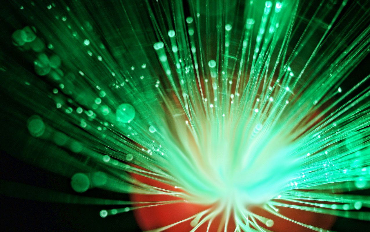 A bundle of illuminated fiber optic strands glowing green and white against a dark background
