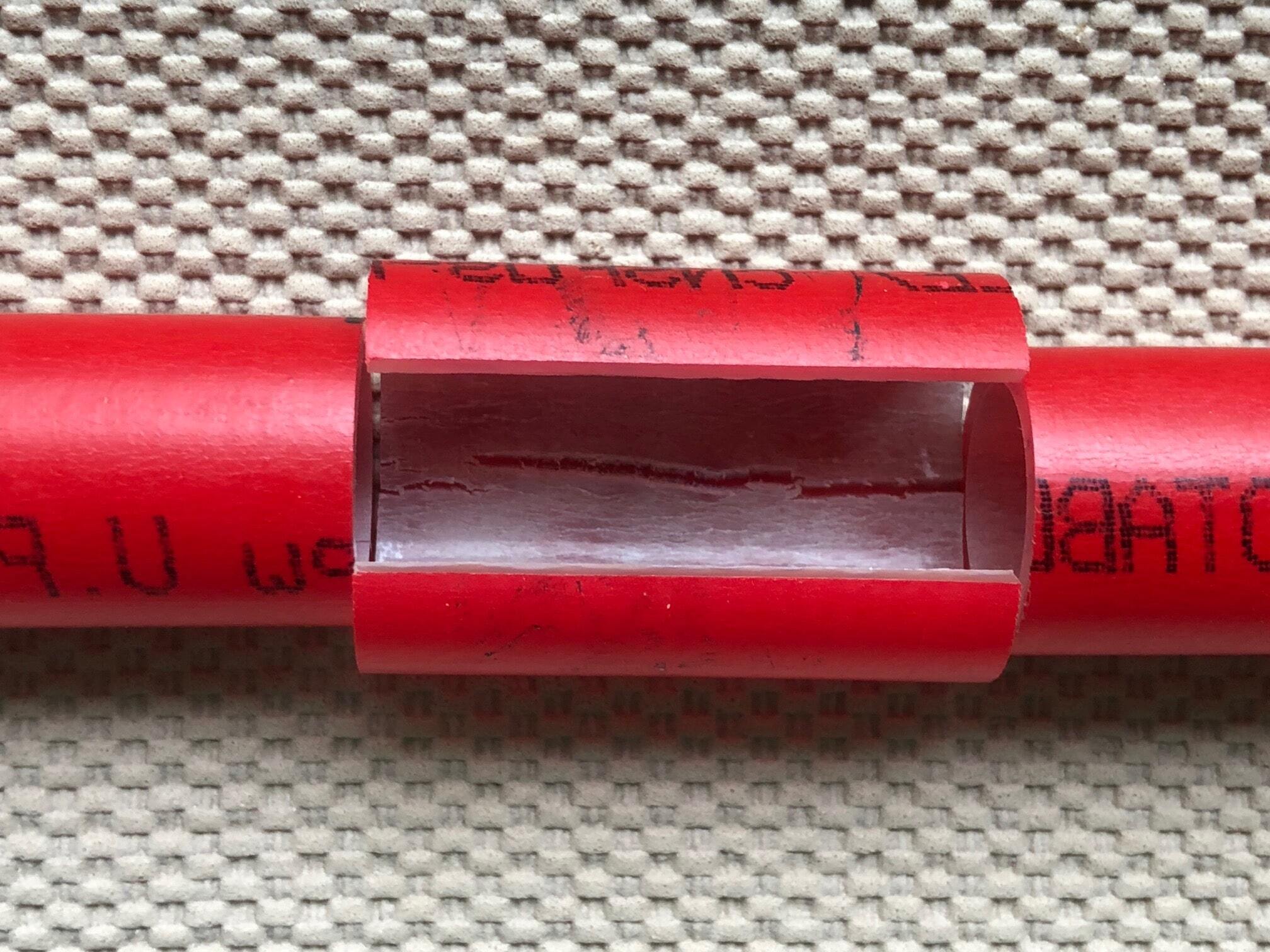A red PEX tube with a window cut through its wall, exposing a longitudinal crack running along the inner surface