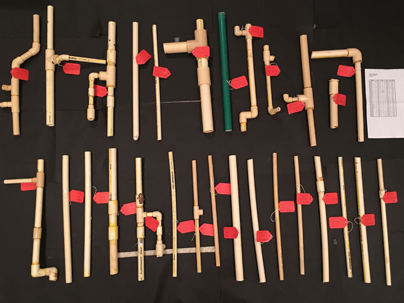 An array of CPVC pipe and fitting assemblies with orange-red fittings, laid out in rows on a dark board