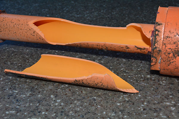 Two curved tan CPVC pipe fragments split lengthwise, laid on a cardboard surface