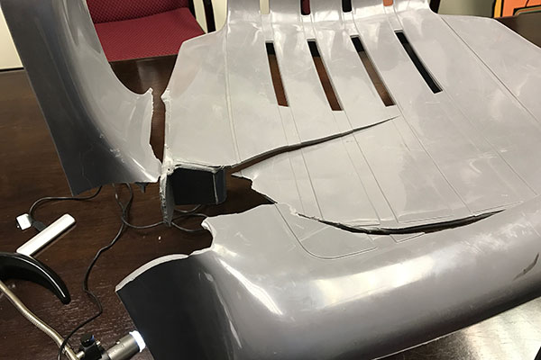 Close-up of a moulded plastic chair component with a dark fracture, indicated with a pointer