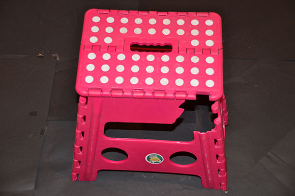 A red folding plastic step stool with a perforated top, photographed from above