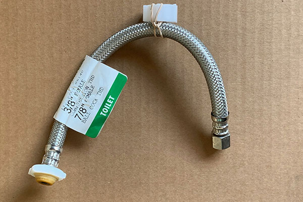 A braided stainless steel toilet supply connector with a white plastic nut and an attached evidence tag