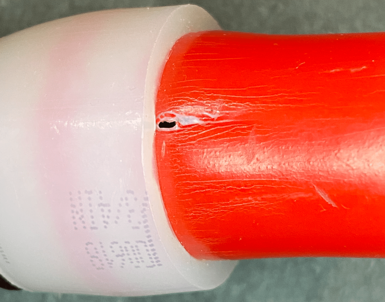 Close-up of a red PEX pipe joined to a white plastic expansion fitting, with a small dark leak hole visible in the fitting collar