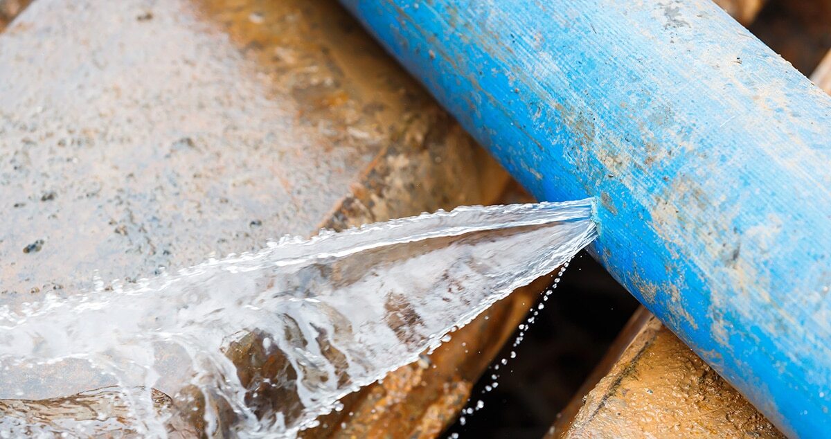 Water spraying from a crack in a corroded blue plastic water pipe
