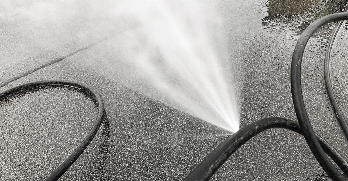 Water spraying out in a fan from a leak on wet asphalt, with dark hoses coiled nearby