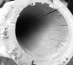 View down the bore of a polypropylene pipe showing a rough, flaking inner surface with radiating cracks after exposure to hot chlorinated water