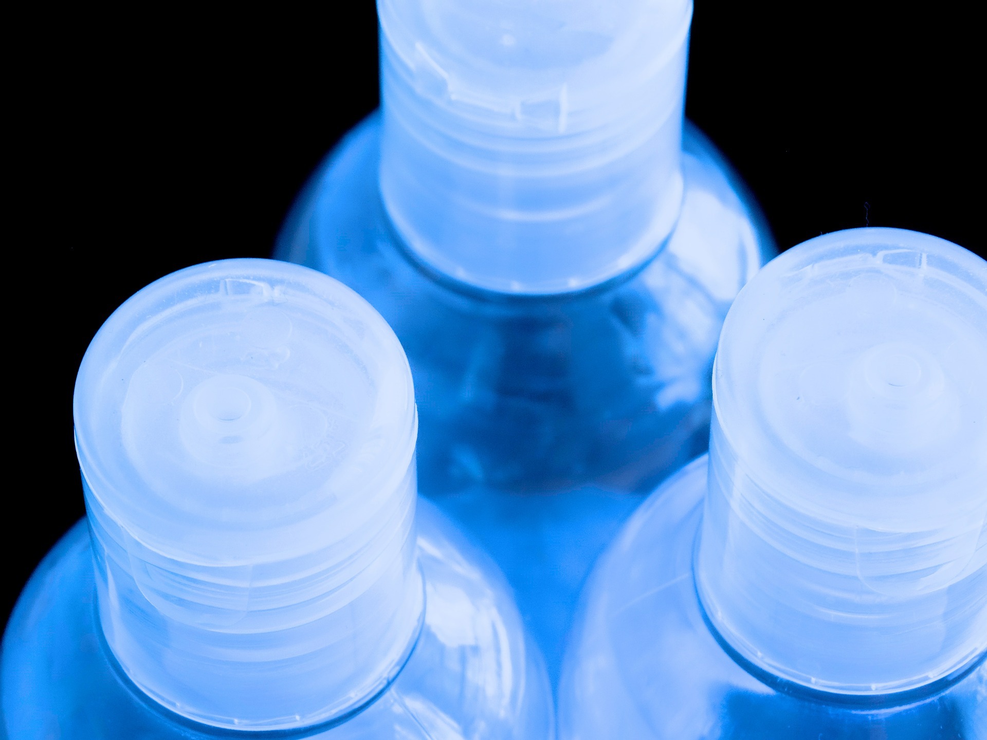 Translucent plastic bottles with ribbed screw caps, lit in blue against a dark background