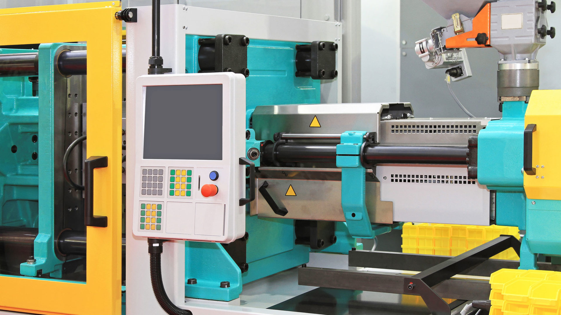 A teal and yellow injection moulding machine with a control panel and material hopper on a factory floor